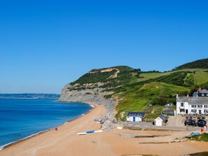 Un hôtel situé sur la côte, avec une plage, une colline verdoyante et un ciel bleu dégagé.