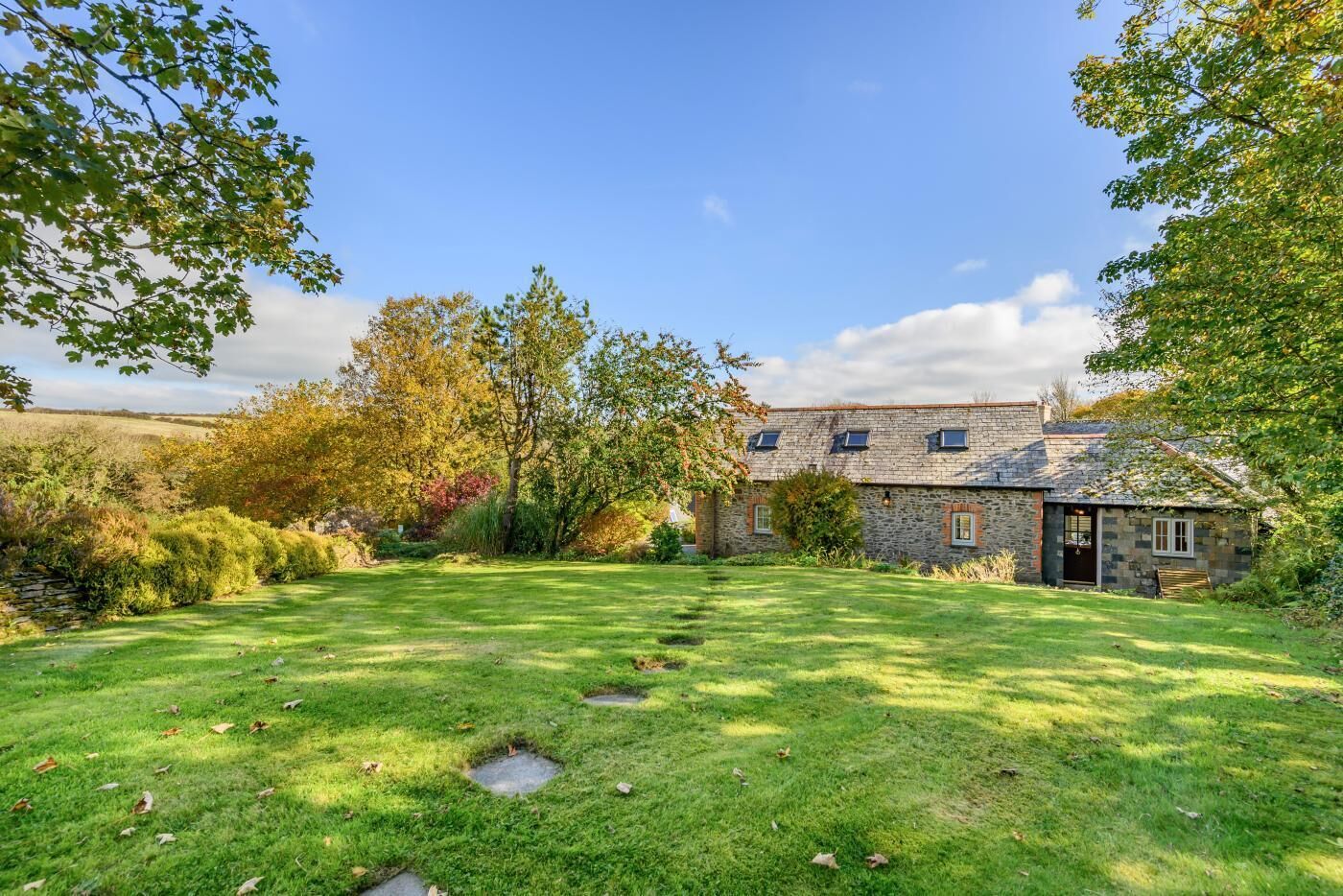 A stone house with a sloped roof, surrounded by a well-maintained lawn and trees.