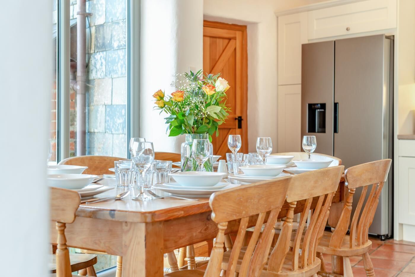 A dining table set for six with white plates, glasses, and a vase of flowers.