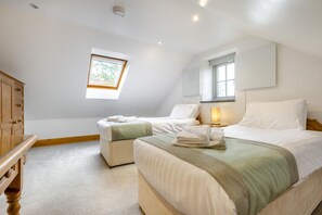Ein Schlafzimmer mit zwei Betten, einer Holzkommode, einem Dachfenster und einer Nachttischlampe.