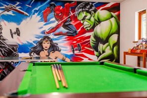 Ein Billardtisch mit Wandgemälde von Superhelden und einem TischtennisSchläger.