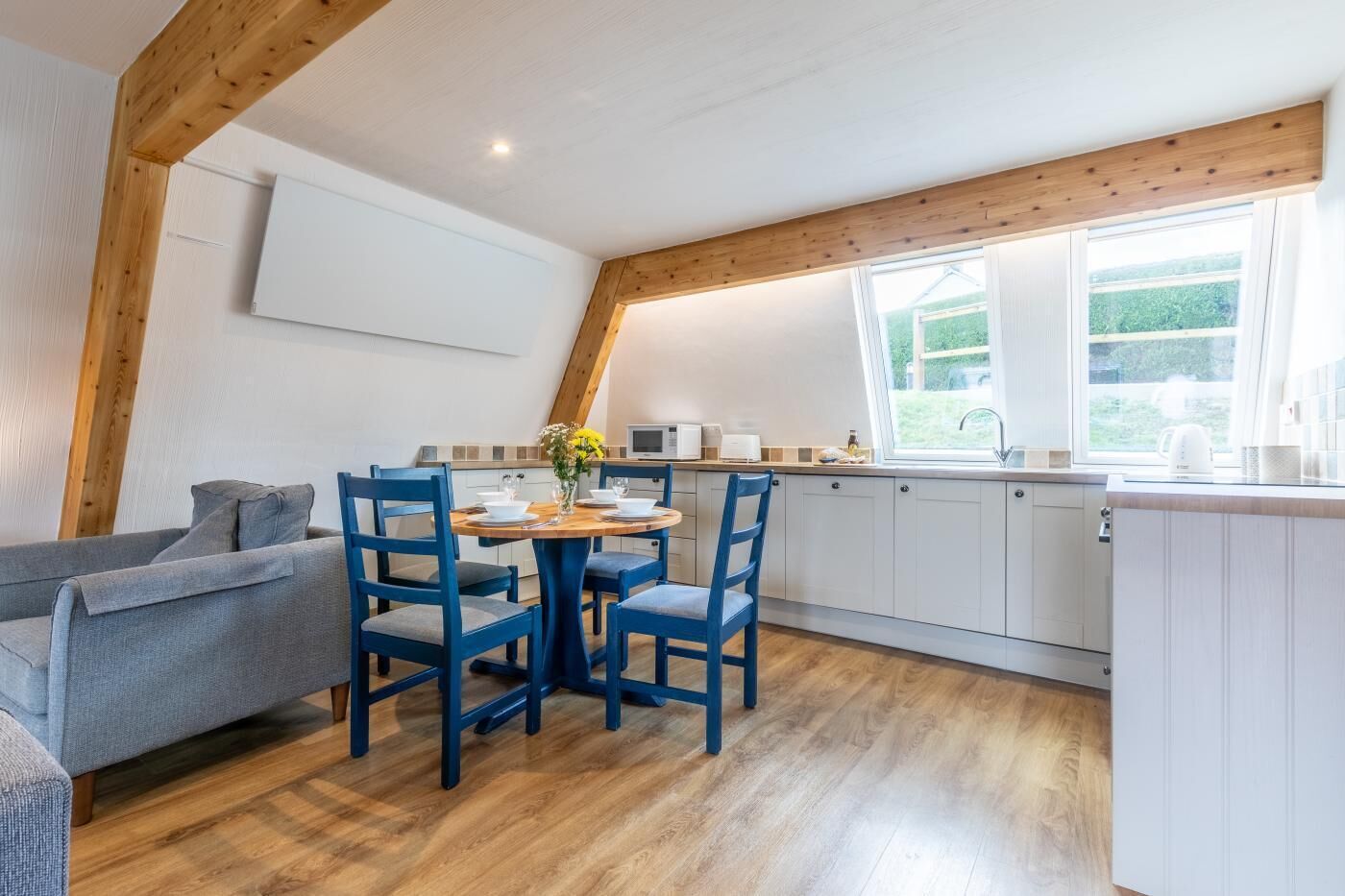 Een moderne keuken met witte kastjes, een houten eettafel met blauwe stoelen en een groot raam dat voor natuurlijk licht zorgt.