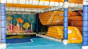Ein Spielbereich für Kinder mit Netzumrandung, bunten Wandmalereien und weichen Spielelementen.