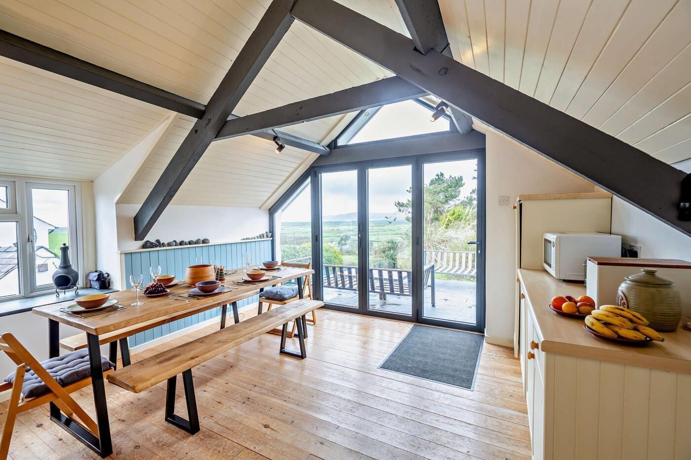 Une cuisine moderne avec une table en bois dressée pour le repas, une grande fenêtre offrant une belle vue et un balcon doté d’une balustrade.