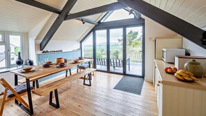 Une cuisine moderne avec une table en bois dressée pour le repas, une grande fenêtre offrant une belle vue et un balcon doté d’une balustrade.