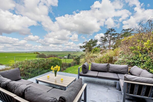 Un espace extérieur aménagé avec un canapé et une table, offrant une vue sur un paysage verdoyant et des champs.