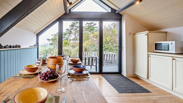 Un espace repas avec une table en bois dressée pour le repas, de grandes fenêtres et une vue sur l’extérieur.