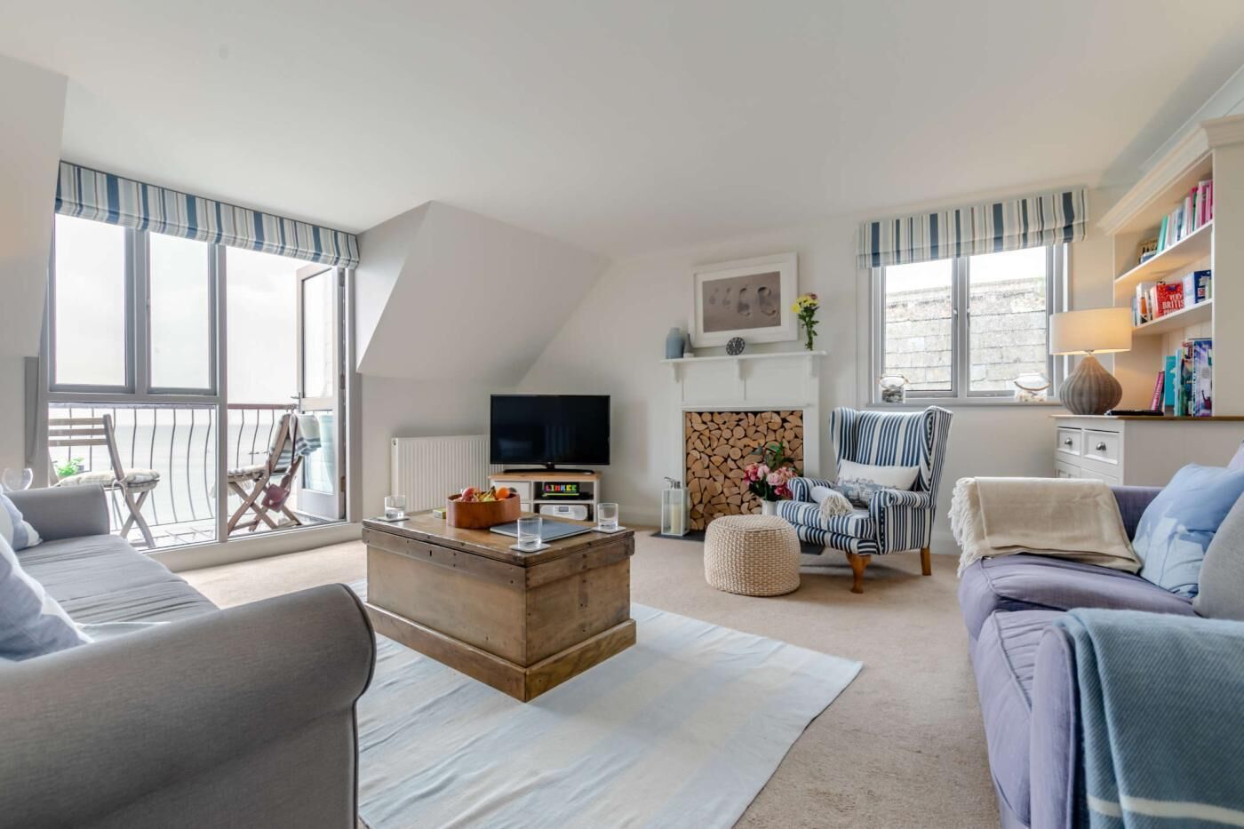 A spacious living room with a large window, a fireplace, a television, and a bookshelf.