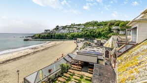 Ein Küstenhotel mit Blick auf den Strand, einer Terrasse mit Sitzgelegenheiten im Freien und einem Hügel mit Gebäuden.