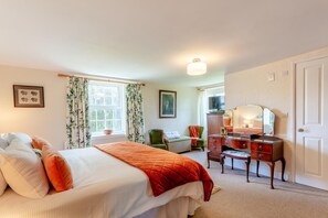 Een slaapkamer met een bed, een dressoir, een stoel, een bureau en een raam met gordijnen.