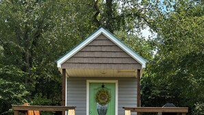 A small wooden structure with a green door, a flower wreath, and a wooden bench outside. - La Petite Maison, Tiny house Melbourne, AR in peaceful community of Mount Olive. (Melbourne)