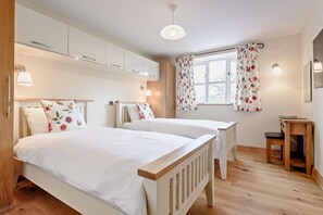 A bedroom with two beds, wooden flooring, a desk, and a window with floral curtains.