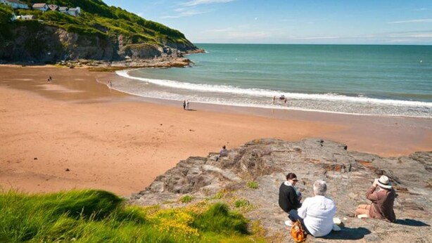 Ein Strand mit felsigem Vordergrund, sandigem Ufer und ruhiger See.