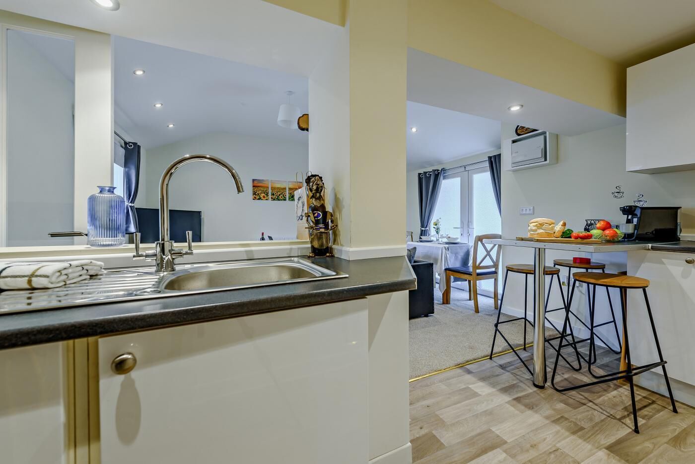 A modern kitchen with a sink, a dining area with a table and chairs, and a view of the living room.