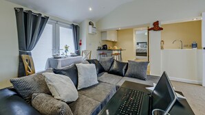Ein modernes Wohnzimmer mit einer Sofagarnitur, einem Esstisch und einem Laptop auf einem Schreibtisch.
