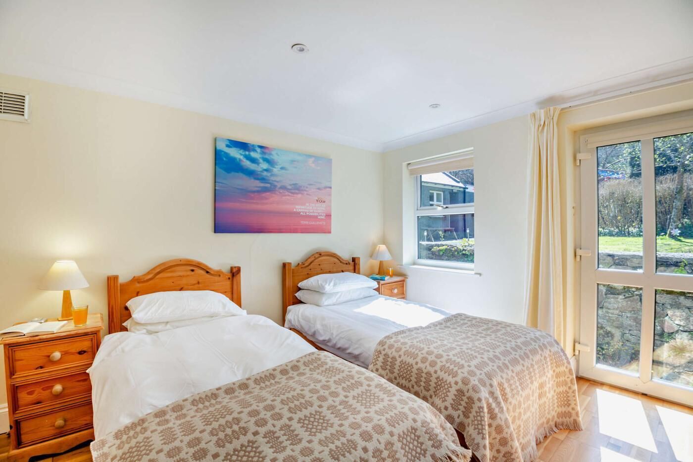 A bedroom with two beds, a window with a view, and a painting on the wall.
