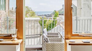 Un balcone con mobili in vimini, un bicchiere d'acqua e vista sul mare e sugli edifici.