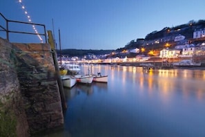 A harbor with boats docked, a stone staircase, and buildings with lights reflecting on the water. - 2 Bed in Looe (oc-b27563) (Looe)