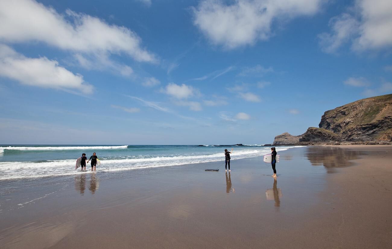 Une plage où l’on voit des gens se promener et porter des planches de surf.