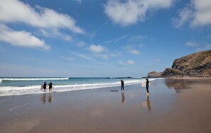 Une plage où l’on voit des gens se promener et porter des planches de surf.