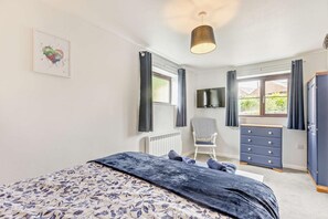 Une chambre à coucher avec un lit, une commode, une chaise et un téléviseur fixé au mur.