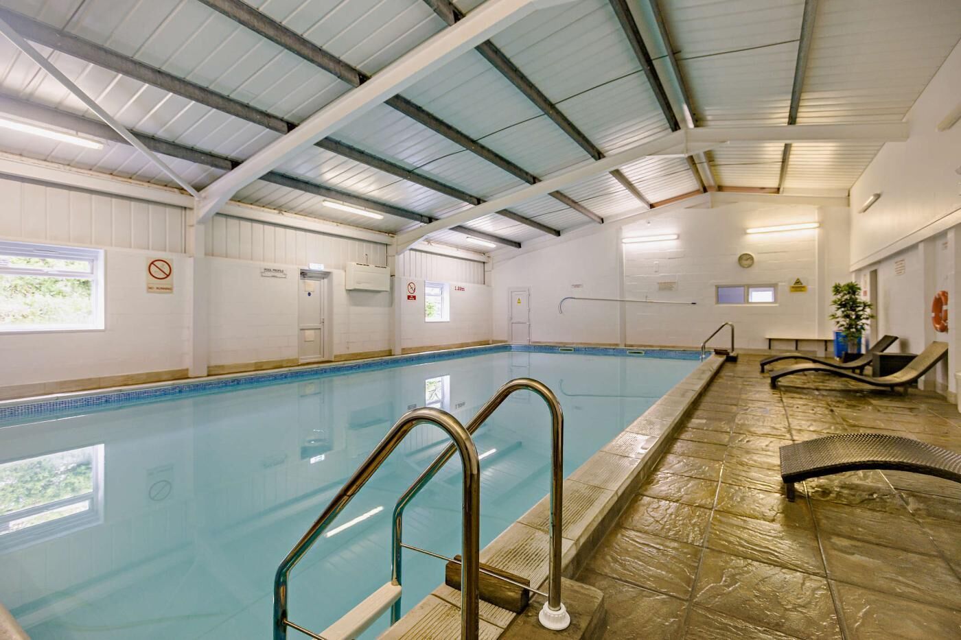 An indoor swimming pool with clear lanes, a lifeguard chair, and a sunshade area.