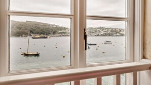 Une vue à travers une fenêtre sur un port, avec des bateaux, une colline et des bâtiments en arrière-plan.