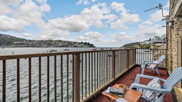Un balcon avec vue sur la mer, une table en bois, deux chaises et un livre intitulé « Guide des oiseaux ».