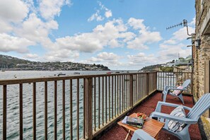 Een balkon met uitzicht op zee, een houten tafel, twee stoelen en een boek getiteld 'Bird Guide'.