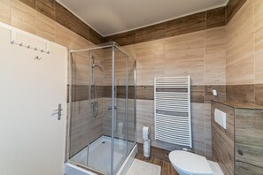 Un baño moderno con ducha acristalada, inodoro blanco y tocador de madera.