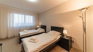 Een hotelkamer met twee bedden, een nachtkastje, een lamp en een raam met gordijnen.
