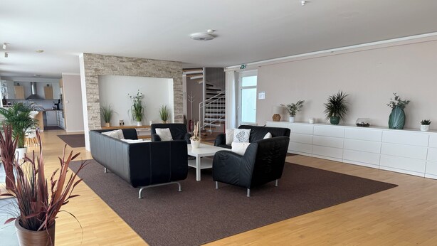 Een moderne woonkamer met een bank, twee fauteuils, een salontafel en een trap naar een verdieping erboven.