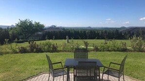 Een terras buiten met een tafel en stoelen, met uitzicht op een grasveld met bomen en heuvels in de verte.