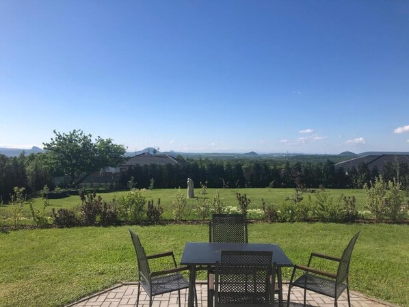 An outdoor patio with a table and chairs, overlooking a grassy area with trees and distant hills. - Penzion Lomská Vyhlídka (Lom)