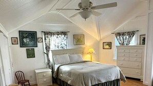 Quarto com cama, mesa de cabeceira, cadeira, cômoda e ventilador de teto.