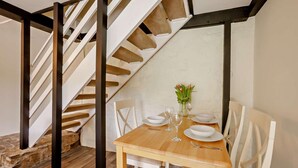 A dining area with a wooden table set for four, white chairs, and a vase with flowers. A staircase with wooden steps and black metal railings is visible in the background. - 2 Bed in Thornbury (oc-r27561) (Thornbury)