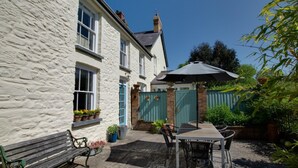 A traditional stone building with a patio area featuring a wooden table and chairs, a bench, and potted plants. - 3 Bed in Aberporth (oc-g27666) (Aberporth)