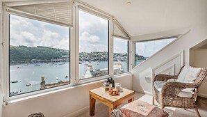Un balcon accueillant avec une table en bois, des chaises en osier et une vue sur un port, avec ses bateaux et ses bâtiments.