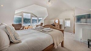 Une chambre à coucher avec un grand lit, une commode en bois, une chaise et un téléviseur fixé au mur.