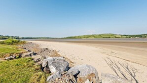 A wide sandy beach with large rocks in the foreground and a clear blue sky. - 4 Bed in Llansteffan (oc-e27710) (Ferryside)