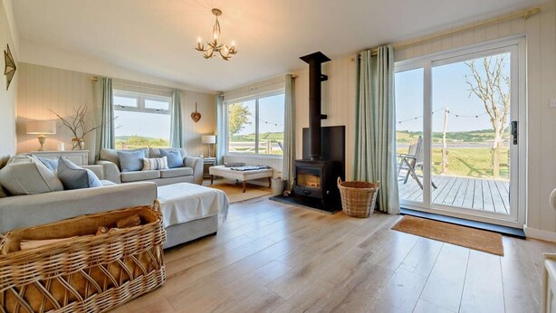A spacious living room with a fireplace, a sofa, a coffee table, and a view of the outdoors. - 4 Bed in Llansteffan (oc-e27710) (Ferryside)