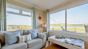 A room with a sofa, a bench, and large windows offering a view of a landscape. - 4 Bed in Llansteffan (oc-e27710) (Ferryside)