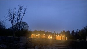 A rustic cabin with a stone foundation, wooden walls, and a porch with string lights. - 4 Bed in Llansteffan (oc-e27710) (Ferryside)