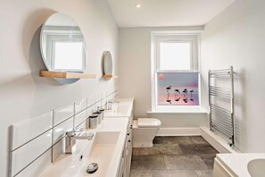 Ein modernes Badezimmer mit großem Spiegel, zwei Waschbecken, Toilette und Fenster mit Sonnenuntergangsblick.