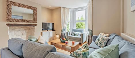 Ein Wohnzimmer mit Kamin, Fernseher, einer Couch, einem Couchtisch und einem Fenster mit Vorhängen.