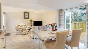 A spacious living room with a white sofa, a dining table set for four, and a large window with a view of the outdoors. - 1 Bed in Welcombe (oc-h27741) (Welcombe)
