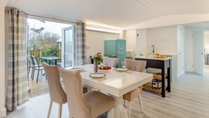 A modern kitchen with a teal refrigerator, a dining area with a white table and beige chairs, and a view of the outdoors through large windows. - 1 Bed in Welcombe (oc-h27741) (Welcombe)