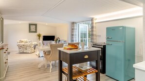 A modern kitchen with a teal refrigerator, a dining area with a white table and chairs, and a living room with a sofa and a TV. - 1 Bed in Welcombe (oc-h27741) (Welcombe)