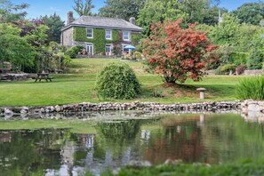 A stone house with ivy-covered walls, a pond, and a well-maintained garden with a variety of plants and a bench. - 3 Bed in Uphill (oc-n27747) (Linkinhorne)