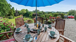 A wooden table set outdoors with a blue umbrella, surrounded by chairs, and various tableware. - 3 Bed in Uphill (oc-n27747) (Linkinhorne)